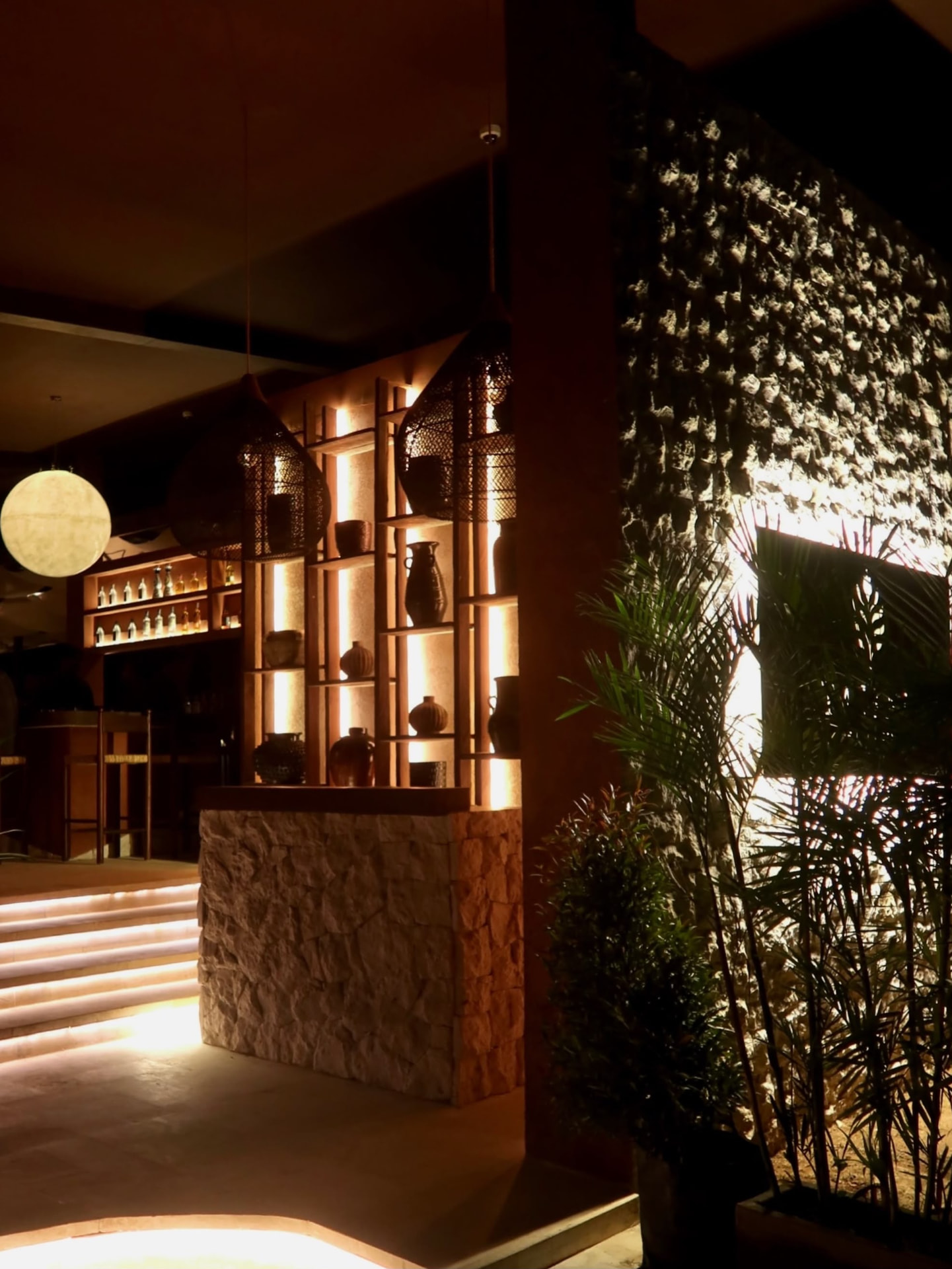 Warm evening entrance to TAMAN with illuminated terracotta walls, pottery and tropical greenery