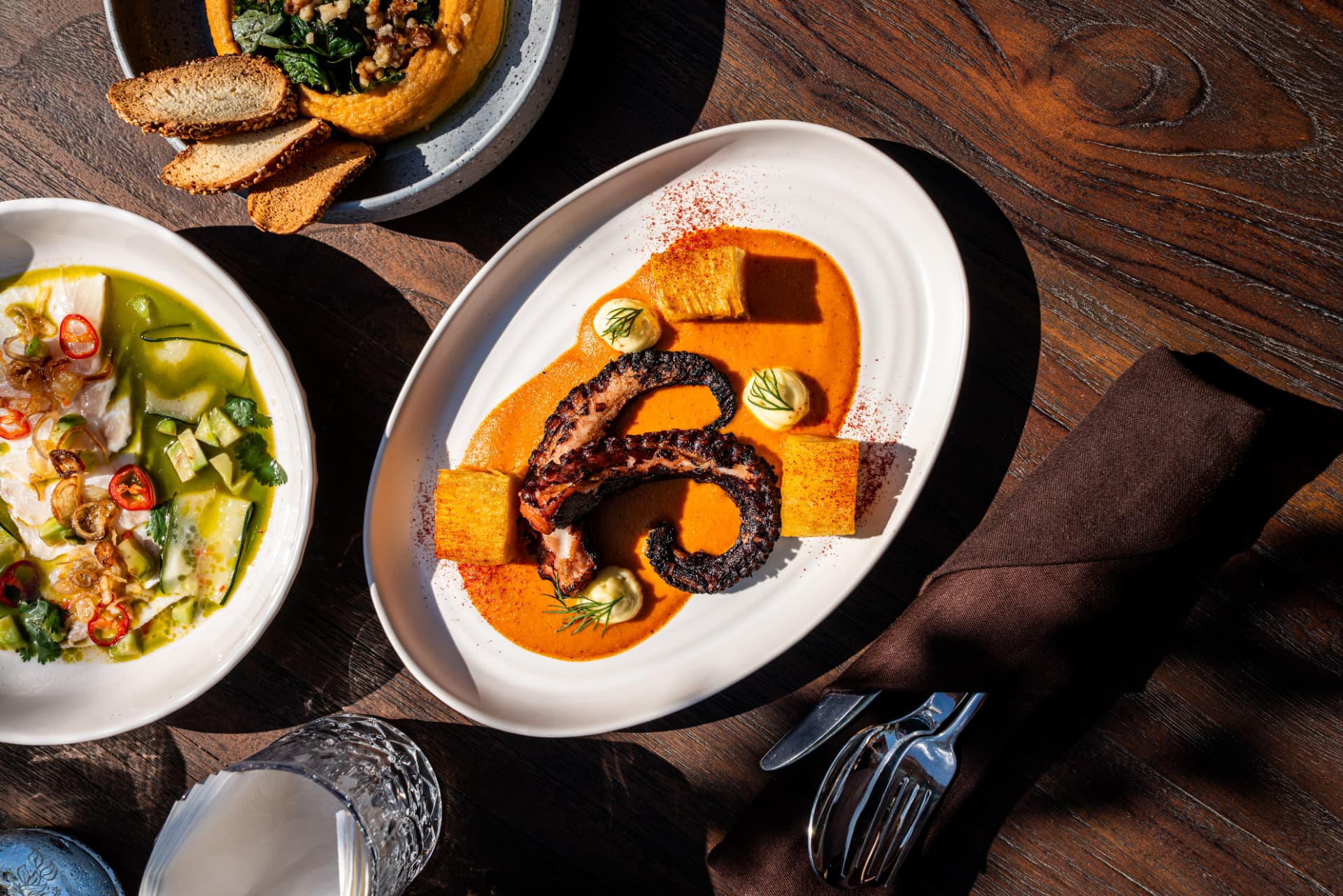 Grilled octopus and colourful shared plates on a wooden table at TAMAN